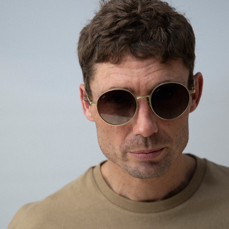 Man wearing round sunglasses with gold frame and grey lenses