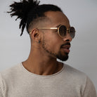 Black man wearing round sunglasses with gold frame and grey lenses looking sideways