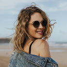 Blonde girl on a beach wearing round sunglasses with gold frame and grey lenses