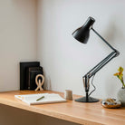 Sleek Anglepoise Type 75 Desk Lamp in Jet Black on a wooden desk with books, pen, and vase, combining style and functionality.