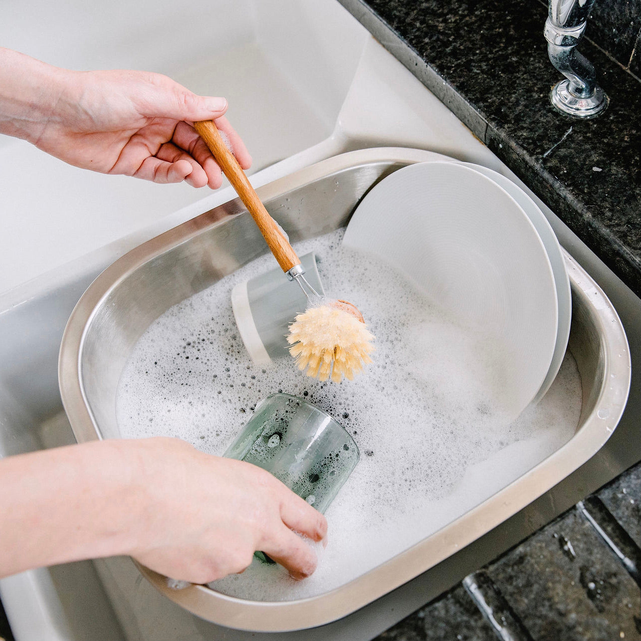 Person washing dishes in a stainless steel washing up bowl.